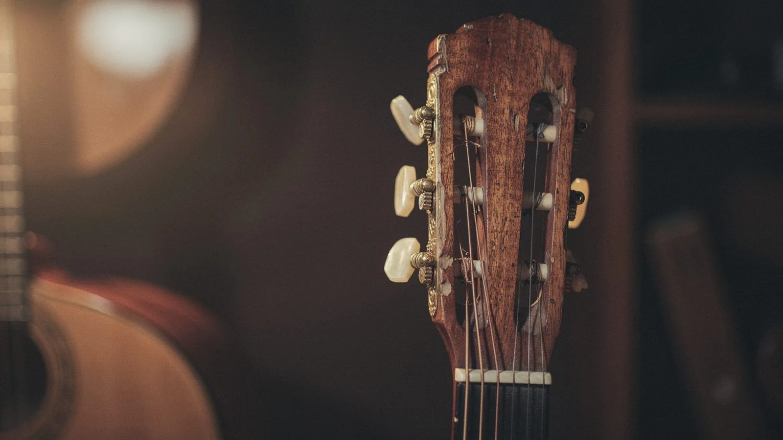 Close-up of a worn cedar nylon-string flamenco guitar headstock with mother-of-pearl tuning pegs, a second guitar dimly visible behind it — the descending bass line of the Andalusian cadence has been the sound of Spanish guitar music for four centuries