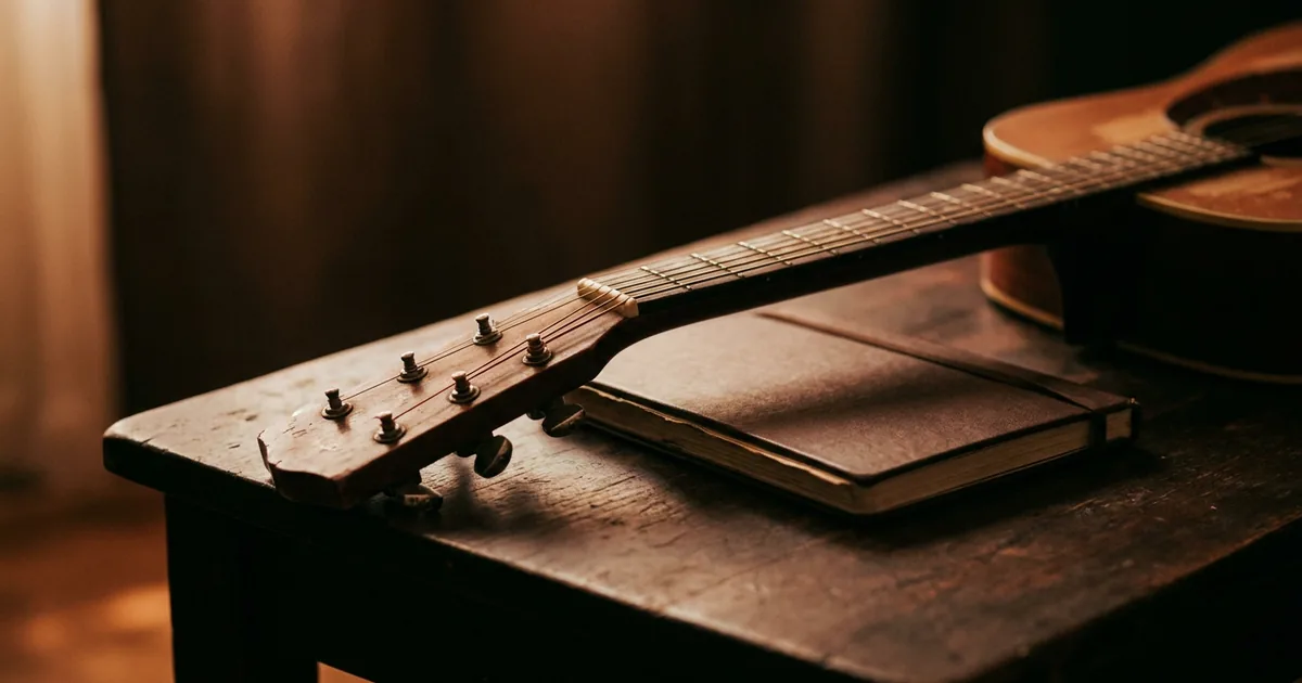 An acoustic guitar neck resting beside a worn hardback notebook, the pre-digital setup for keeping lyric and chord ideas