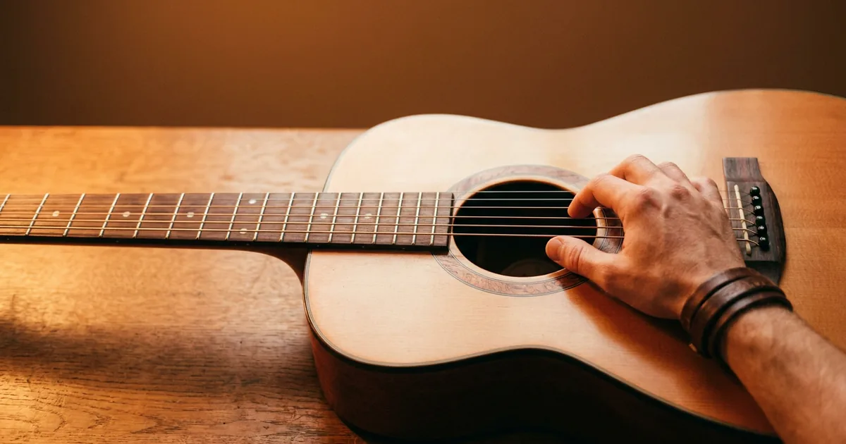 Finding the key of a song on guitar: a songwriter's hand strumming an acoustic guitar lying on a warm oak table, listening for the chord that sounds like home.