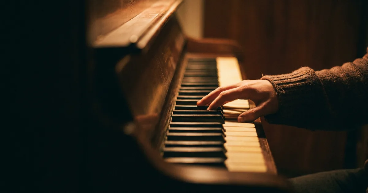 A hand playing a minor chord on the keys of an upright piano in warm low light, illustrating the chords available in a minor key