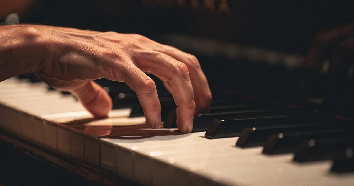 A hand voicing a chord on a piano keyboard in warm amber light, the kind of voicing a songwriter chooses when placing a chord inversion.