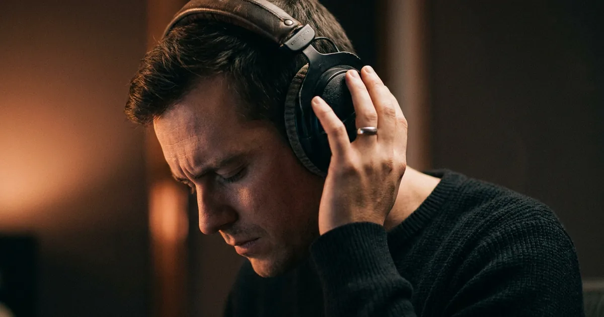 A musician in over-ear headphones listening back to a recording with eyes closed, the close listening it takes to tell whether a song was made with AI