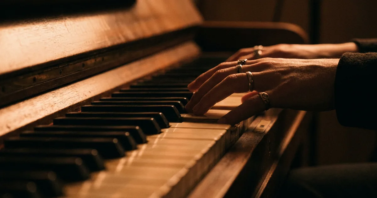Hands playing a warmly lit upright piano, the instrument where many songwriters work out the chords for a song's bridge
